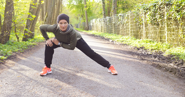 Fitnesstrainerin dehnt Beinmuskulatur auf einem Waldweg