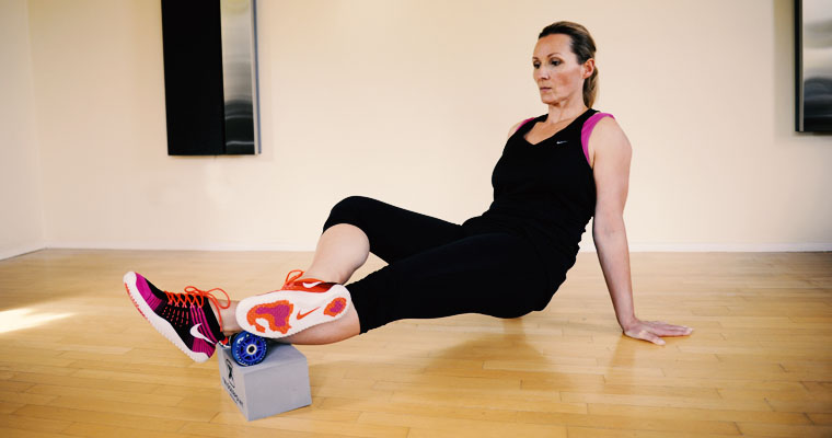 Trainerin rollt mittels Faszienrolle über die Wade